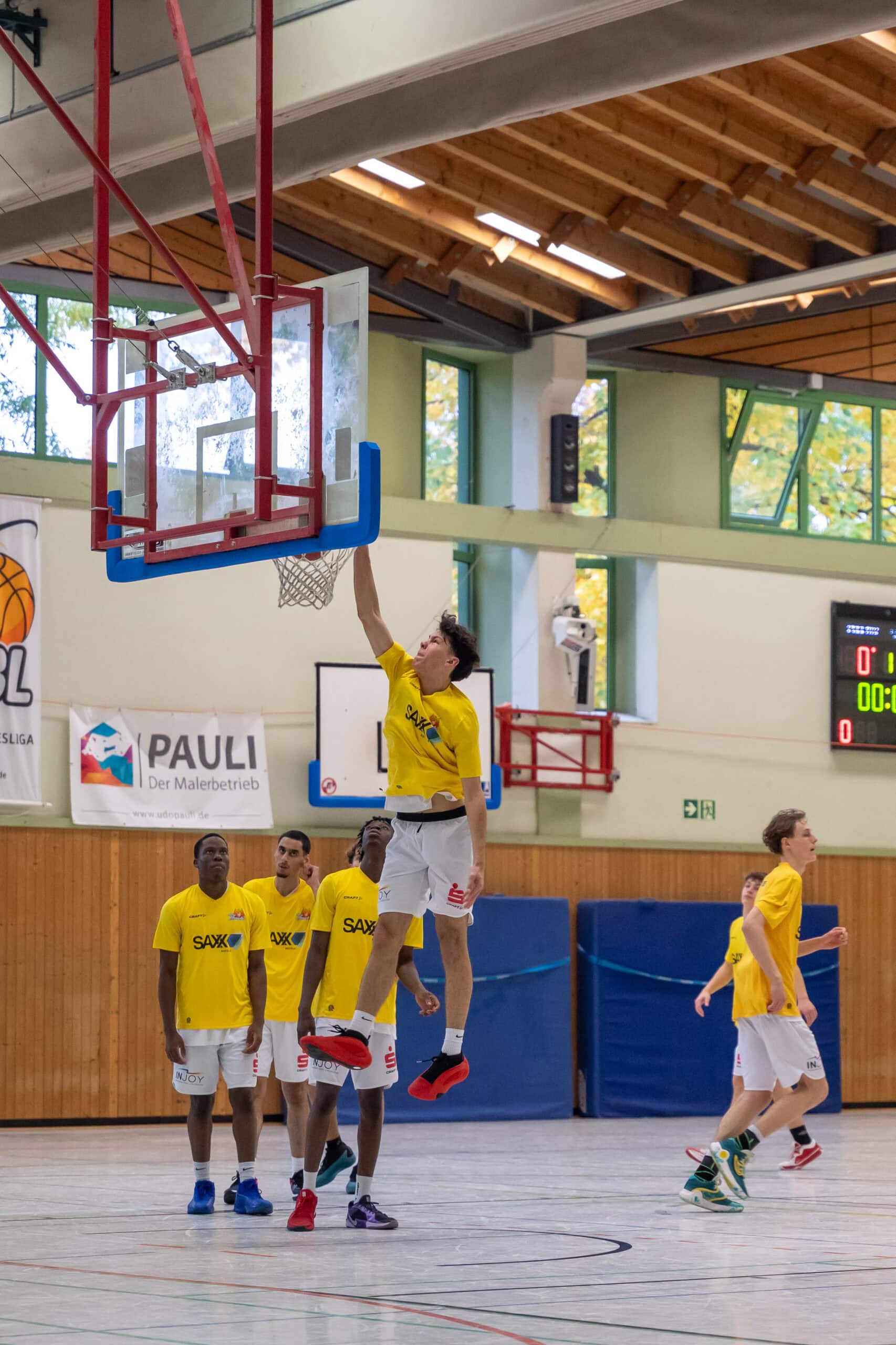 Eine Basketballmannschaft in gelben Trikots übt Korbleger in einer Turnhalle.