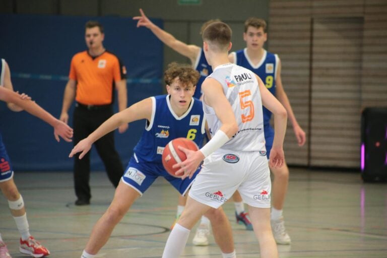 Ein junger Basketballspieler in einem blauen Trikot verteidigt mit konzentriertem Ausdruck.