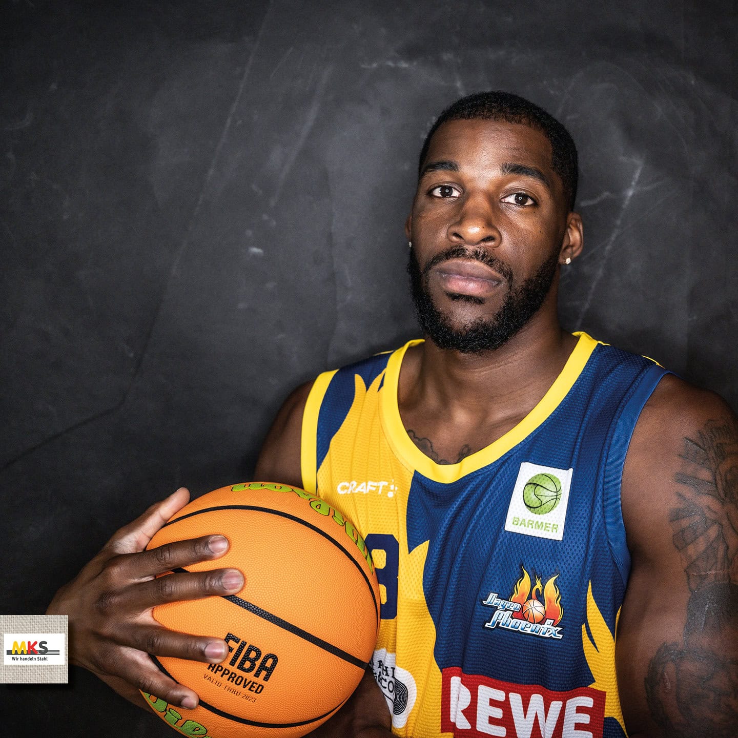 Ein Basketballspieler mit ernster Miene hält einen Ball, trägt ein blau-gelbes Trikot.