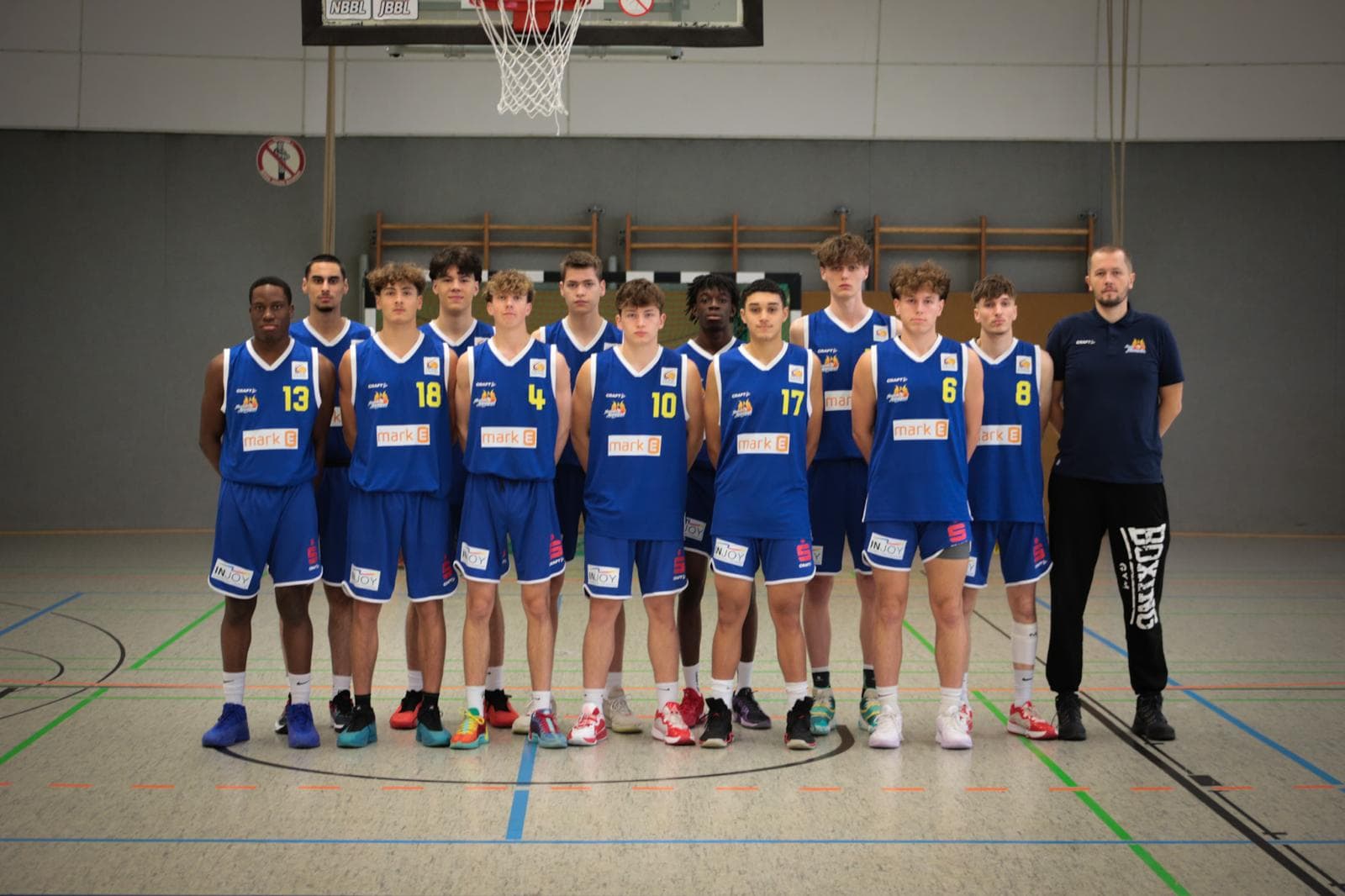 Basketballteam in blauen Trikots, ein Spieler steht neben dem Trainer unter einem Basketballkorb.