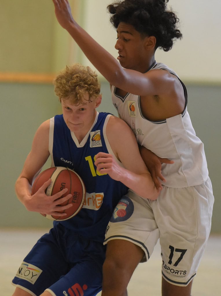 Zwei junge Männer spielen Basketball. Einer dribbelt entschlossen, während der andere verteidigt.