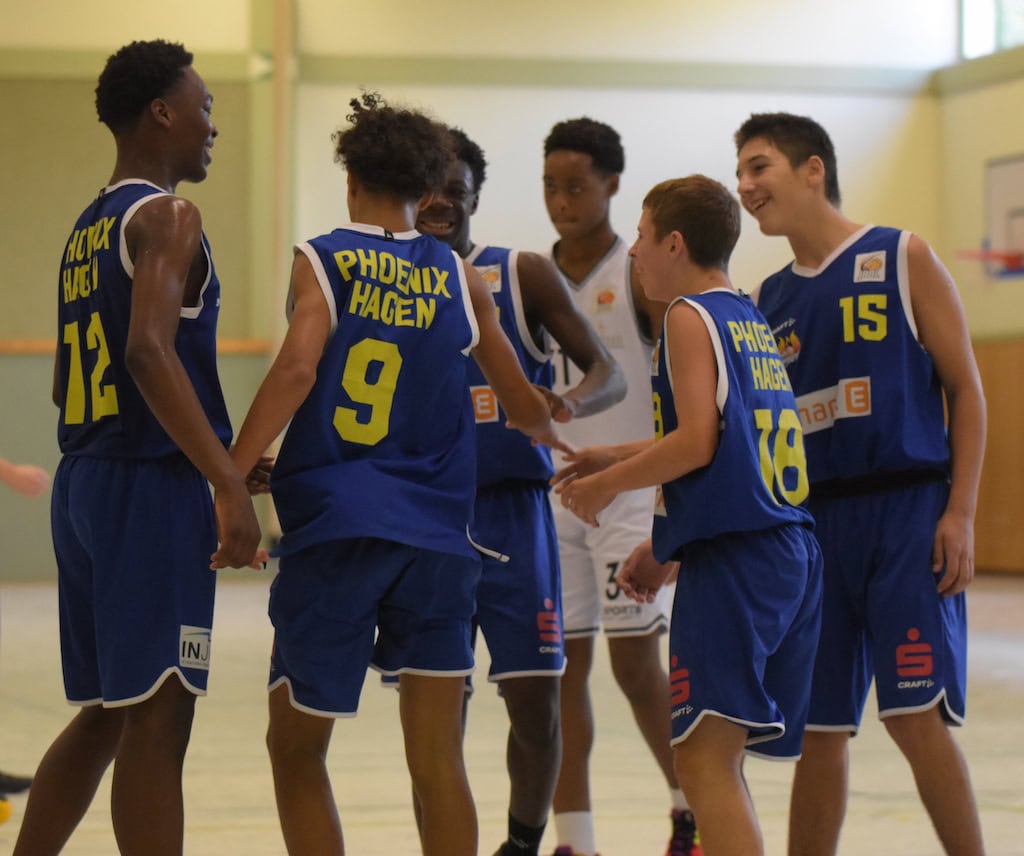 Gruppe von Jugendlichen in blauen Basketballtrikots, lachend und interagierend auf dem Spielfeld.