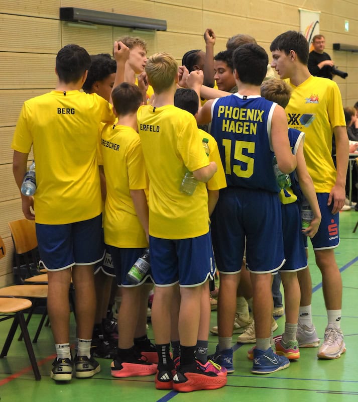 Jugendbasketballteam in gelben und blauen Trikots, hebt freudig die Hände.