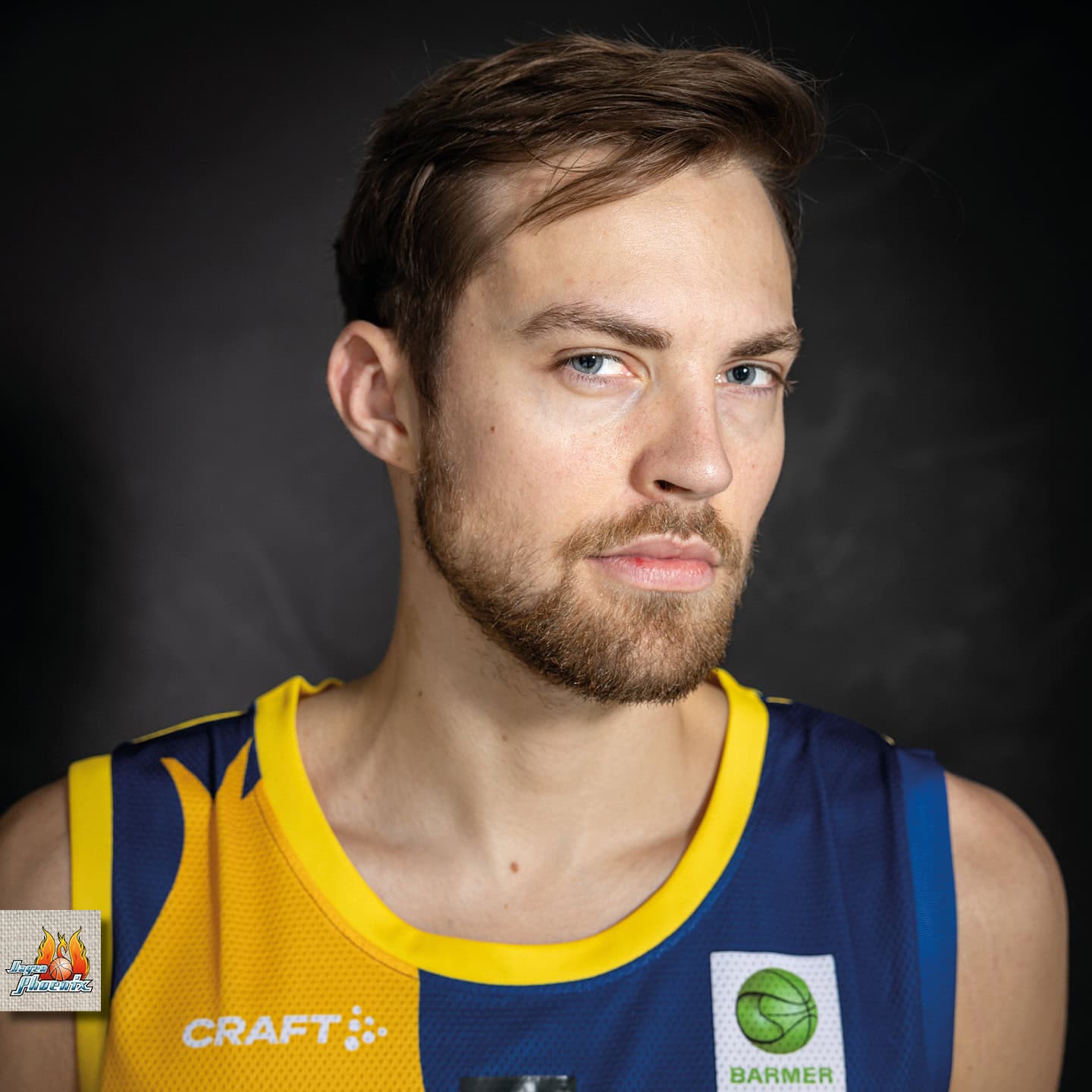 Ein Mann mit ernstem Blick, Bart, kurzen Haaren, trägt ein blau-gelbes Basketballtrikot.