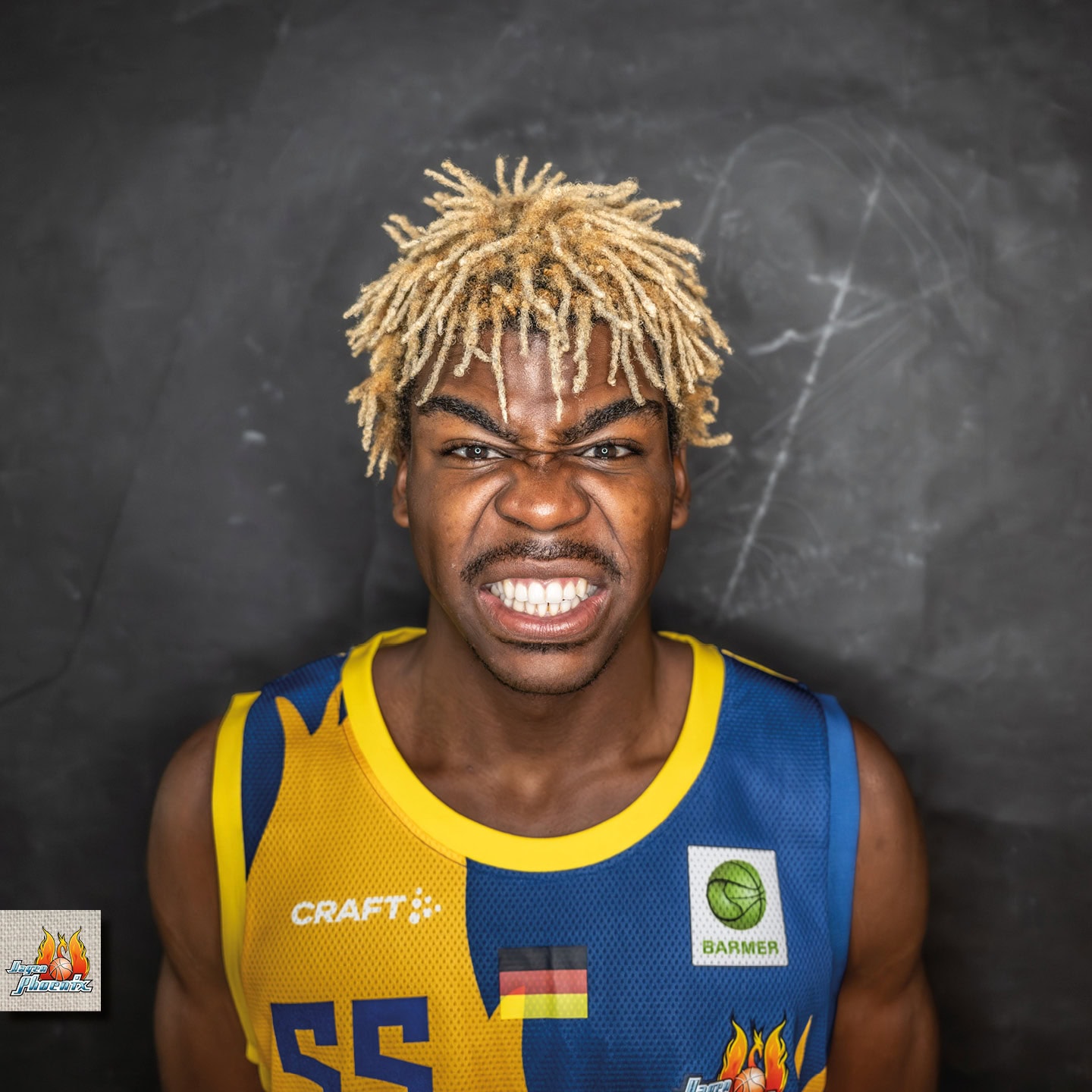 <p lang="de-DE_formal">Junger Mann mit blonden Dreadlocks, grimmiger Gesichtsausdruck, farbenfrohes Basketballtrikot.</p>