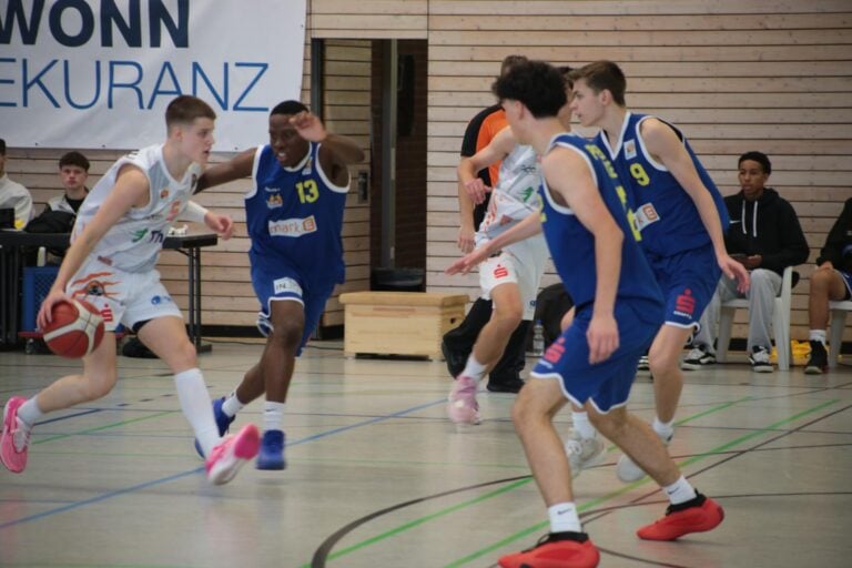 Das Bild zeigt ein Basketballspiel, bei dem ein Spieler in Weiß den Ball dribbelt.