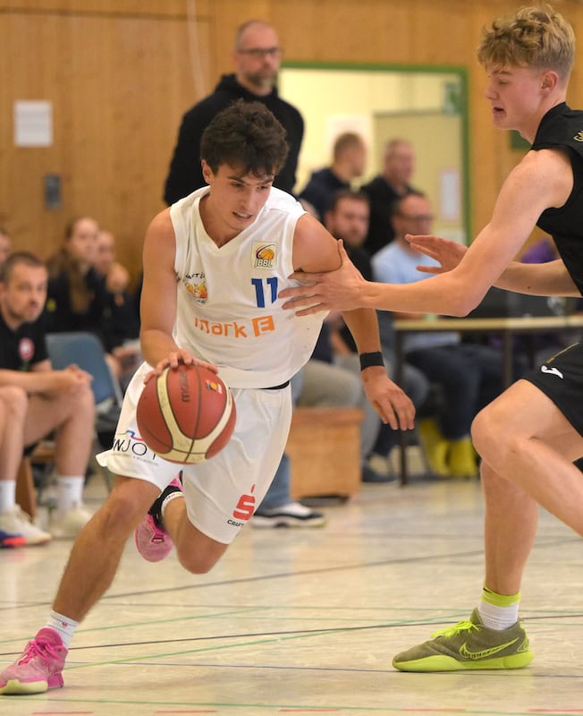 Ein jugendlicher Basketballspieler im weißen Trikot dribbelt, während ein Gegner ihn verteidigt.