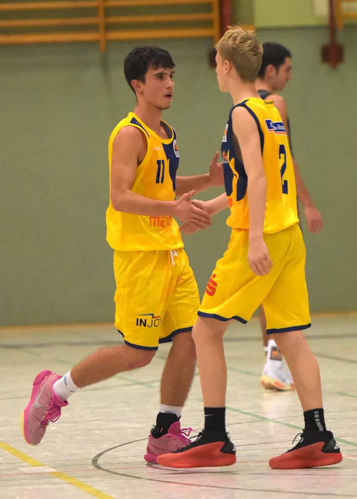 Zwei junge Männer in gelben Basketballtrikots begrüßen sich auf dem Spielfeld.