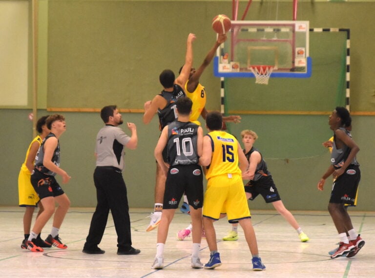 Basketballspiel mit Spielern in grauen und gelben Trikots bei Ballwurf; energetische Szene.