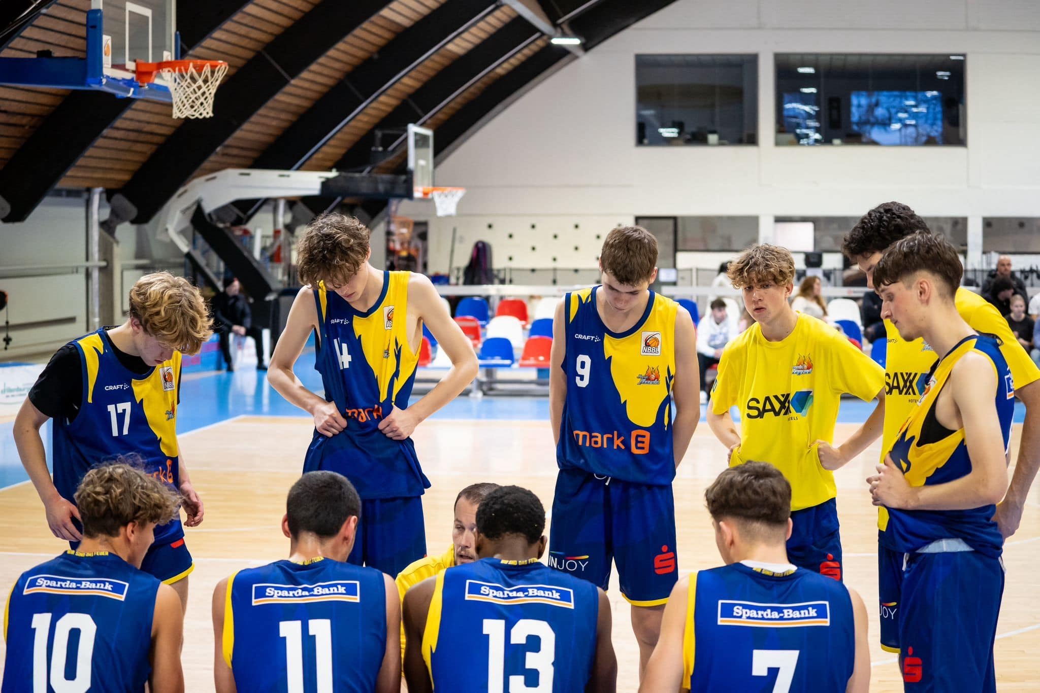 Basketballteam in blauen Trikots bespricht sich ernsthaft auf dem Spielfeld unter einem Bogen.