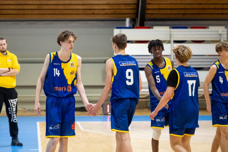 Fünf Basketballspieler in blauen Trikots, fröhlich, auf dem Spielfeld beim Abklatschen.