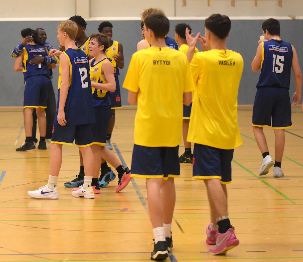 Basketballspieler in blauen und gelben Trikots jubeln auf dem Spielfeld.