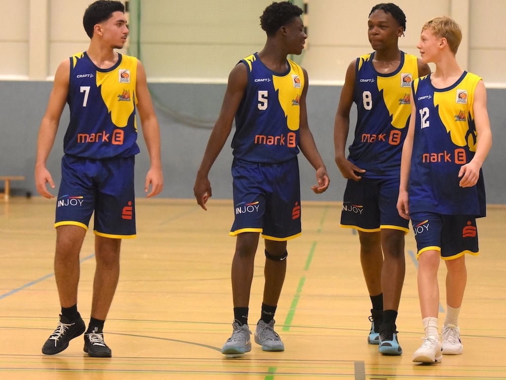 Vier junge Basketballspieler in blauen Trikots gehen lächelnd über das Spielfeld.