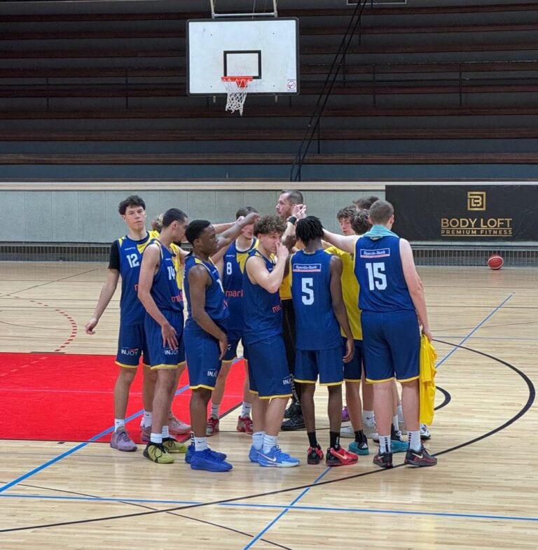 Eine Gruppe von Basketballspielern in blauen Trikots diskutiert auf dem Spielfeld.