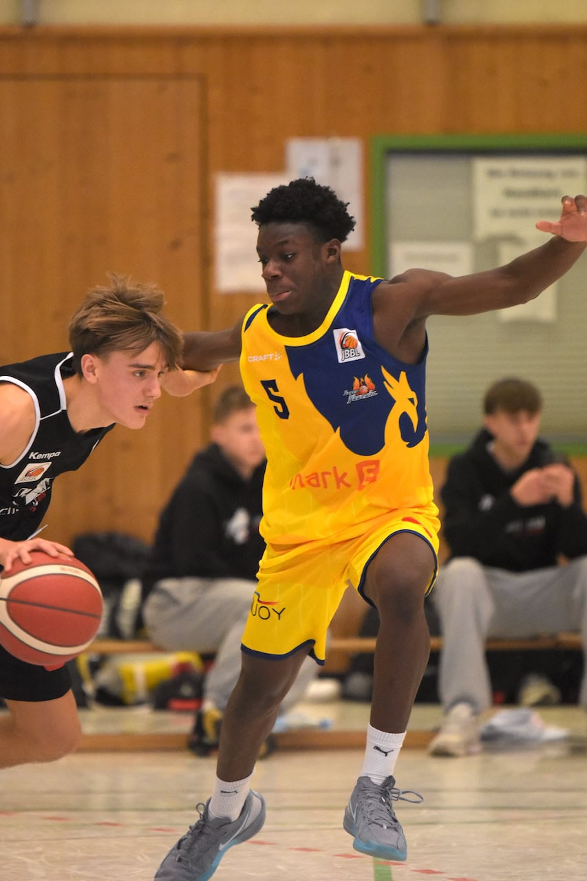 Ein junger, entschlossener Basketballspieler im gelb-blauen Trikot verteidigt energisch.