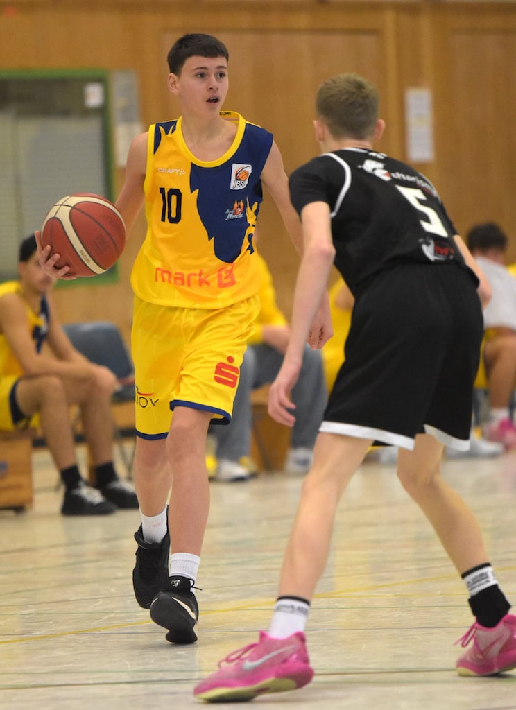 Basketballspieler im gelben Trikot dribbelt den Ball, steht vor Gegenspieler im schwarzen Trikot.