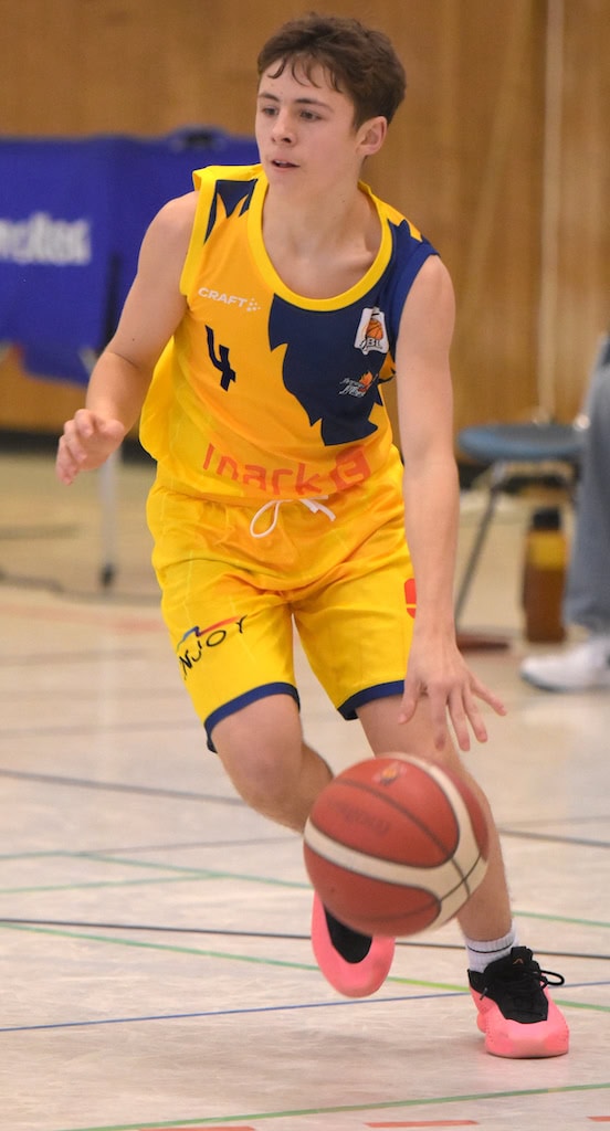 Junger Basketballspieler in gelbem Trikot dribbelt konzentriert einen rot-weißen Basketball.