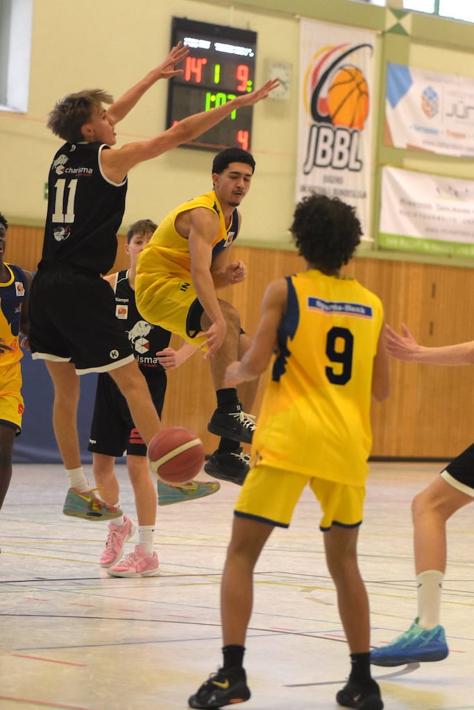 Basketballspieler in gelben Trikots kämpfen um den Ball auf einem Spielfeld unter Schildern.