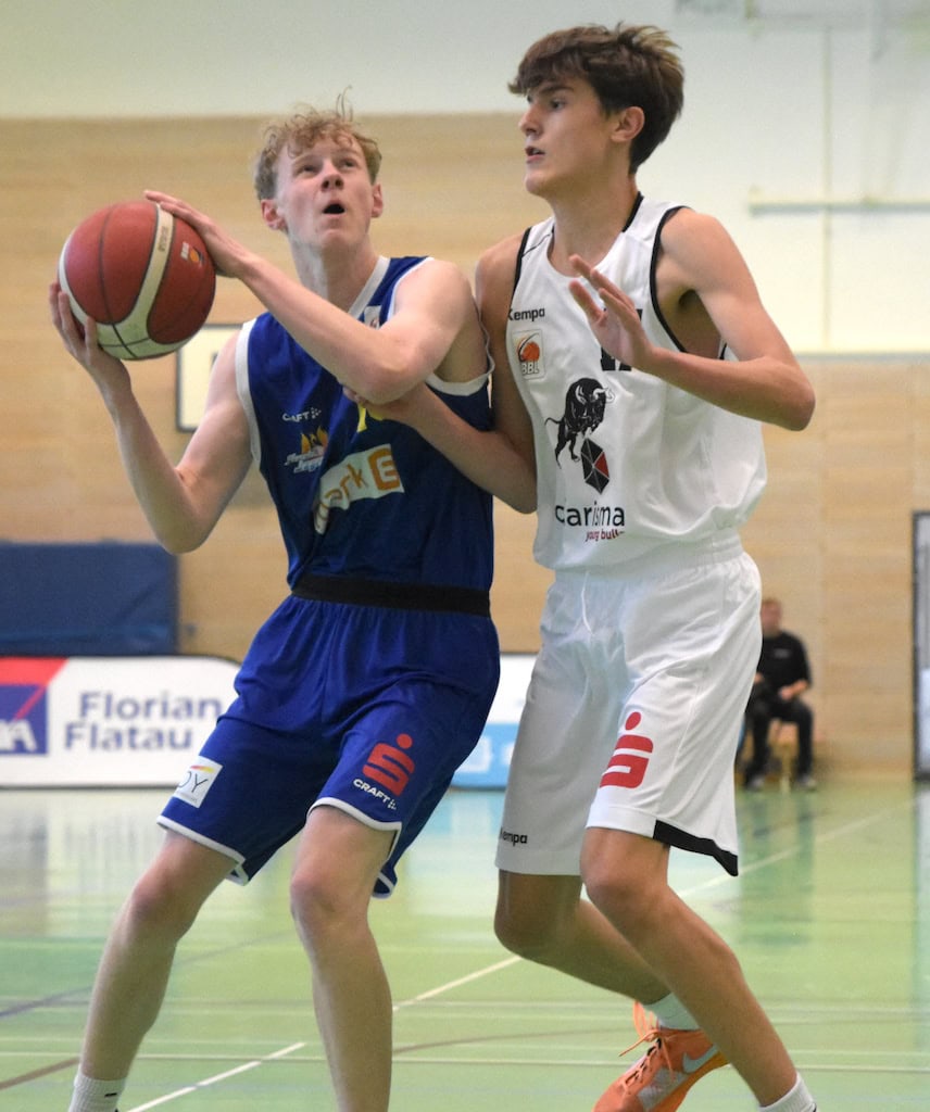 Zwei junge Basketballspieler im Spiel, einer in blauem, der andere in weißem Trikot, konzentriert.