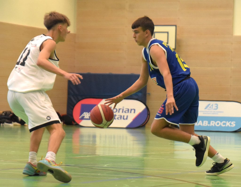 Zwei junge Basketballspieler im Spiel, intensiver Gesichtsausdruck, einer in blau, der andere in weiß.