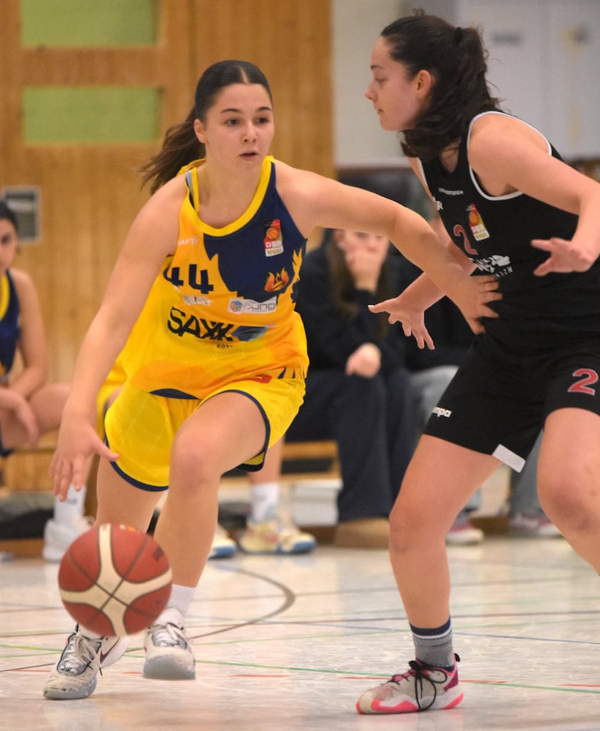 Zwei weibliche Basketballspielerinnen im Spiel: gelbes Trikot dribbelt, schwarzes Trikot verteidigt.