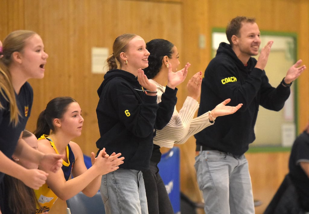 Gruppe Jugendliche und Trainer in Sporthalle klatschen begeistert, tragen sportliche Kleidung.