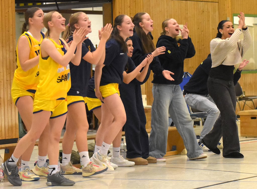 Eine Gruppe junger Frauen in gelben Basketballtrikots jubelt am Spielfeldrand begeistert.