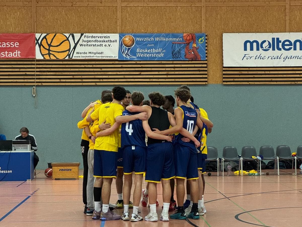 Eine Gruppe von Basketballspielern umarmt sich in einem Hallenspielfeld.