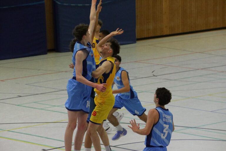 Basketballspiel mit Spielern in blauem und gelbem Trikot in akrobatischen Sprungbewegungen.