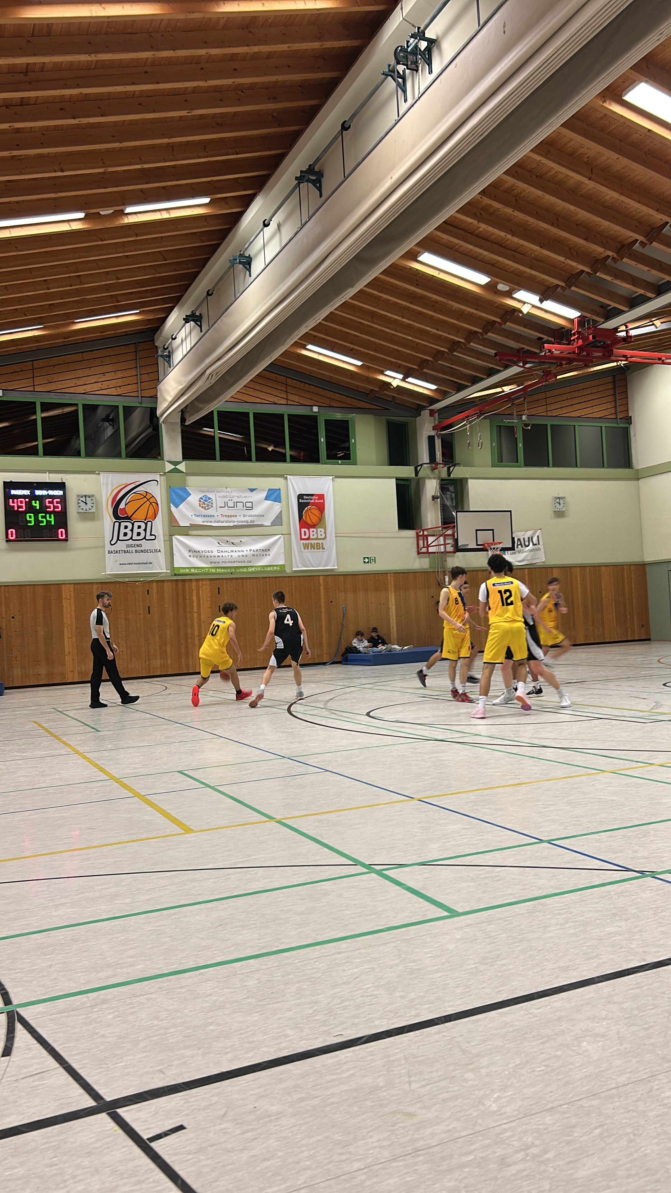 Basketballspiel in der Sporthalle; Team in gelben Trikots spielt gegen ein anderes Team.