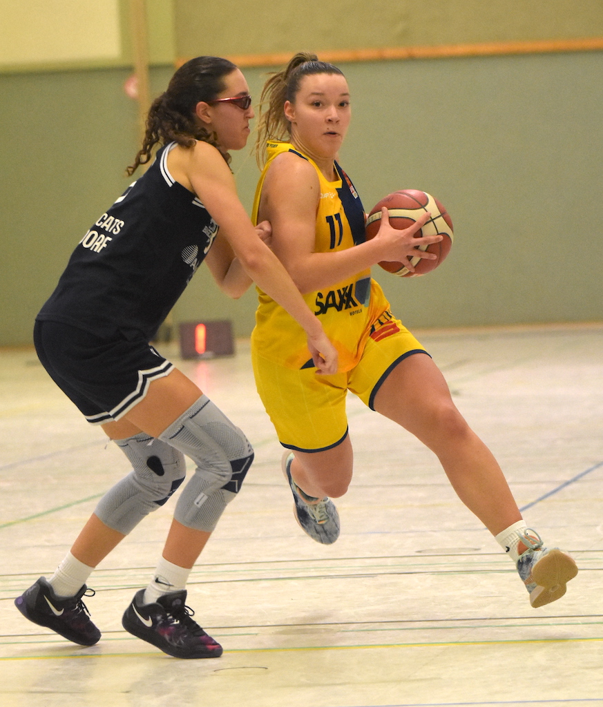 Zwei Basketballspielerinnen im Spiel, konzentriert, gelbes und schwarzes Trikot, sportliche Haltung.