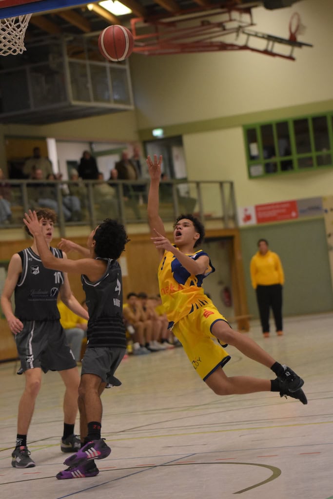 Eine Person in gelbem Basketballtrikot springt nach einem Ballwurf, sichtbar dynamische Geste.