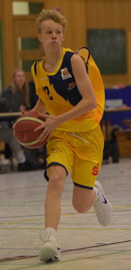 Ein junger Basketballspieler im gelben Trikot konzentriert mit Ball in Bewegung.