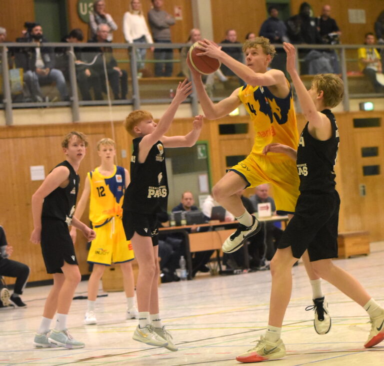 Ein junger Basketballspieler in gelbem Trikot springt und hält den Ball in einem Spiel hoch.