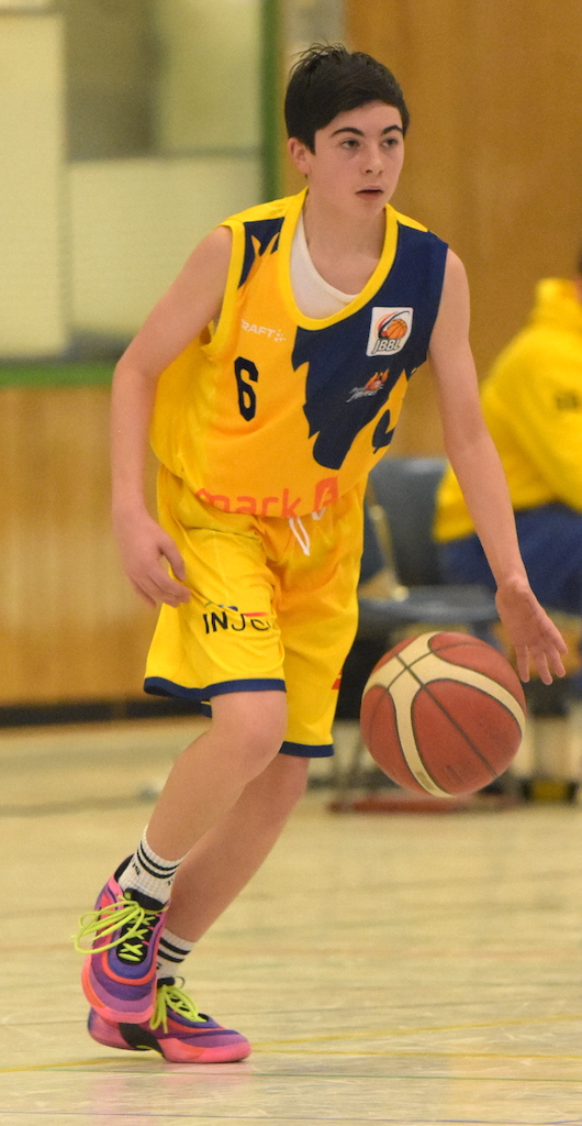 Ein junger Basketballspieler in gelbem Trikot dribbelt den Ball, fokussierter Ausdruck.