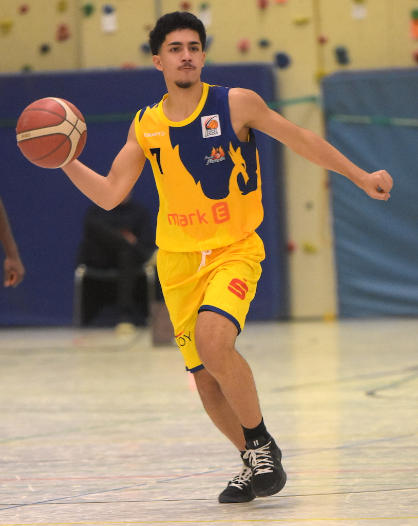 Ein Basketballspieler dribbelt konzentriert, trägt ein gelbes Trikot mit blauen Details.