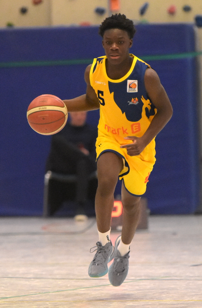 Ein junger Basketballspieler im gelben Trikot dribbelt konzentriert einen Ball auf dem Spielfeld.