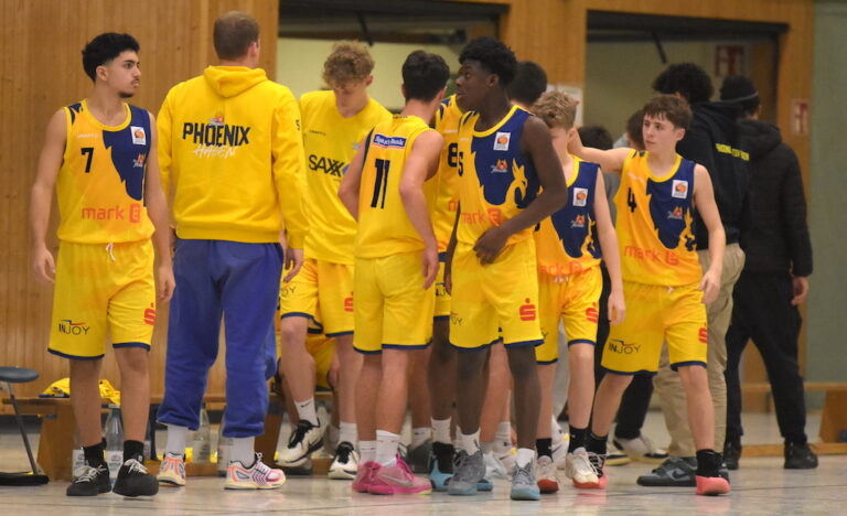 Basketballteam in gelben Trikots, Trainer in gelbem Hoodie, besprechen Taktik in der Halle.