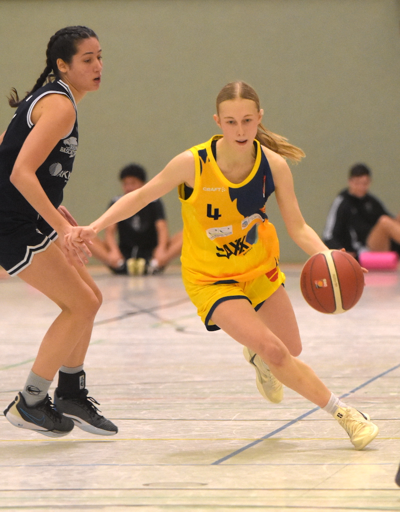 Eine junge Frau im gelben Trikot dribbelt den Basketball, gefolgt von einer Frau im schwarzen Trikot.