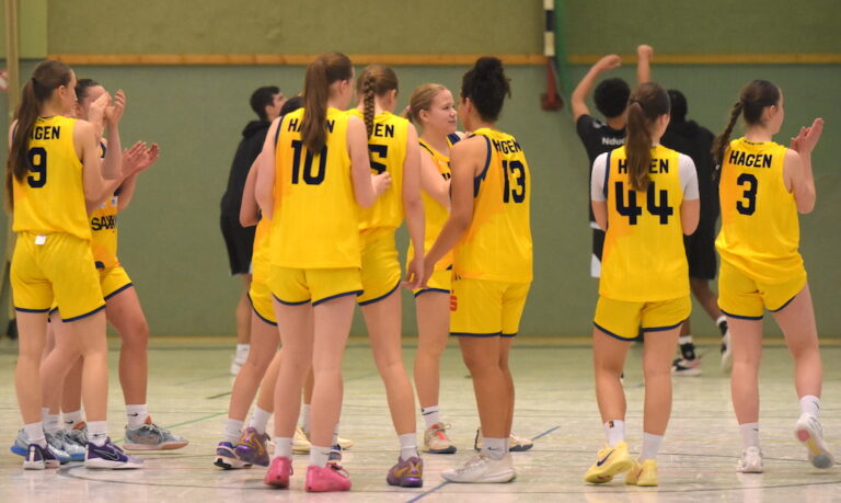 Gruppe von Basketballspielerinnen in gelben Trikots, die applaudieren, in einer Sporthalle.