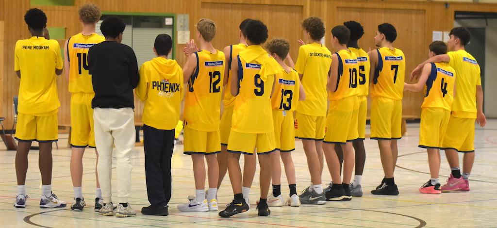 Basketballteam in gelben Trikots, steht in einer Turnhalle, alle schauen von der Kamera weg.