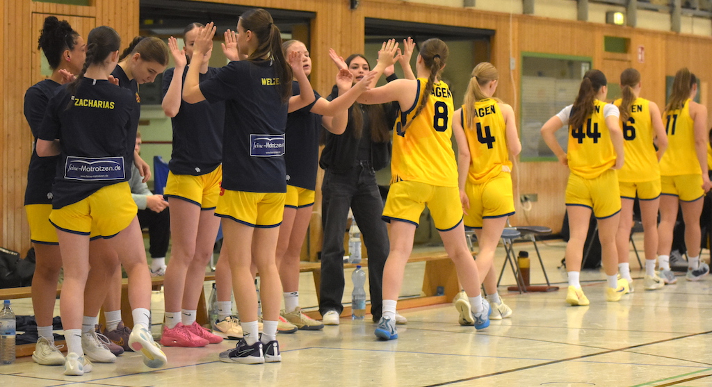 Basketballspielerinnen in gelben Trikots geben High-Fives, lächelnd, in einer Turnhalle.