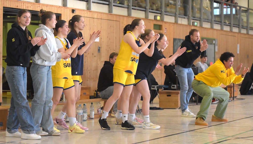 Mehrere jubelnde Personen am Spielfeldrand, tragen gelbe und schwarze Sportkleidung.