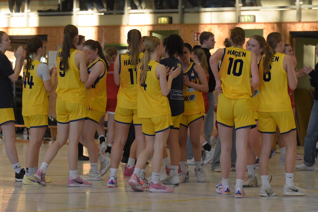 Frauen-Basketballteam in gelben Trikots im Kreis, glücklich und feiernd auf dem Spielfeld.