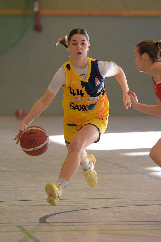 Frau dribbelt Basketball in gelbem Trikot konzentriert, mit Zopf, voller Bewegung.