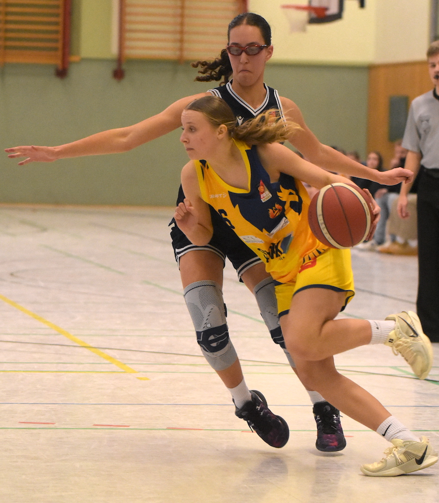 Zwei Basketballspielerinnen; eine mit gelbem Trikot dribbelt den Ball konzentriert vorbei an einer anderen.