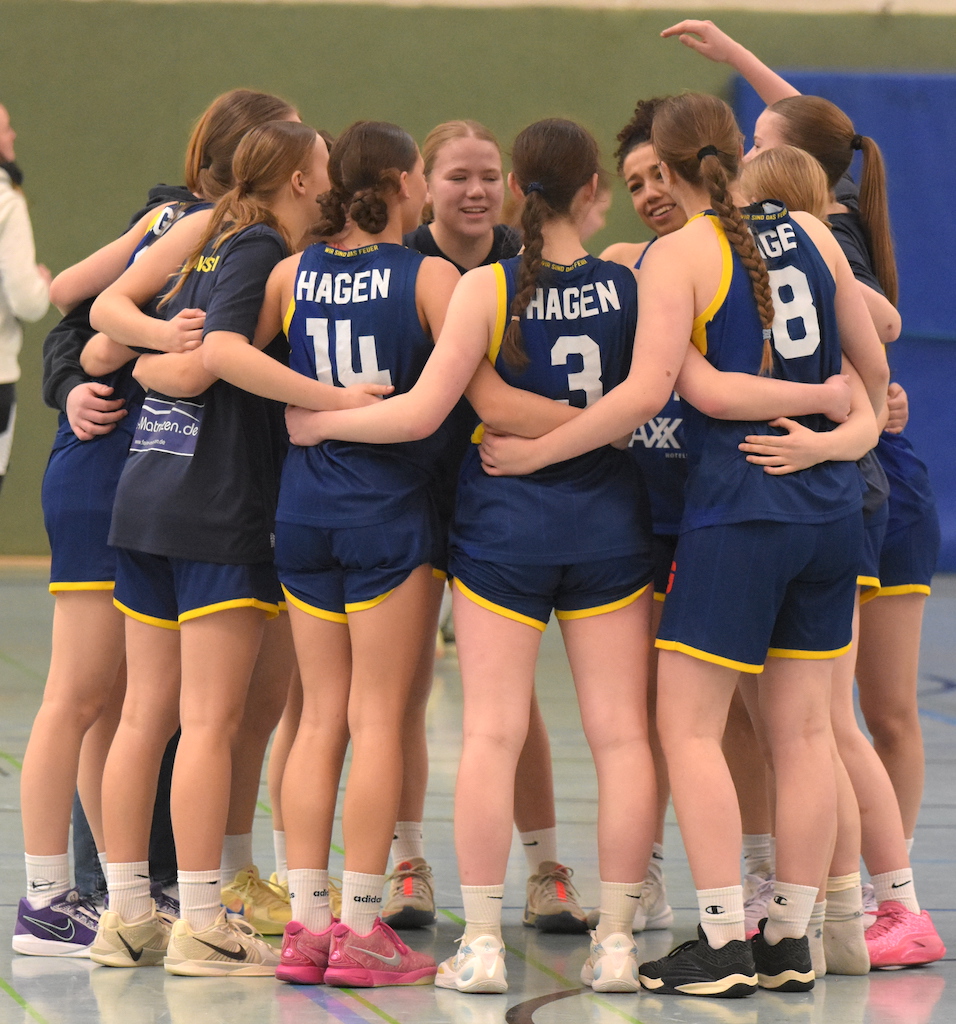 Eine Basketballmannschaft in blauen Trikots jubelt im Kreis, alle fröhlich und motiviert.