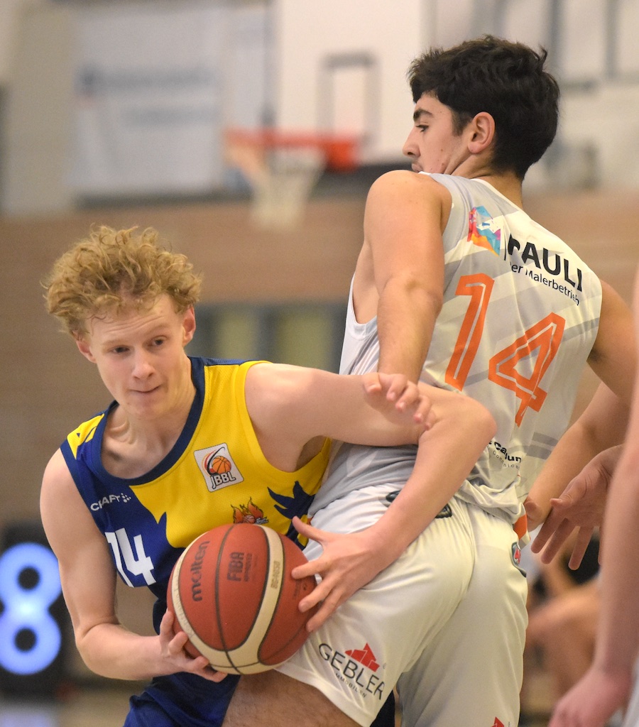 Spieler im blauen Trikot kämpft gegen Spieler im weißen Trikot um den Basketball.