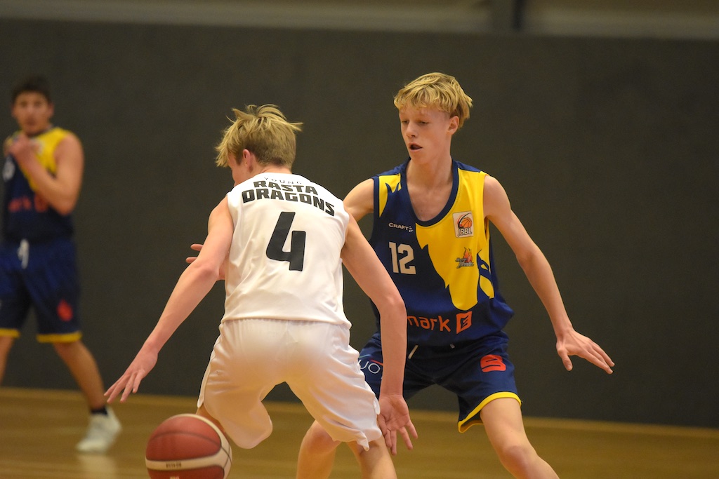 Zwei junge Basketballspieler, konzentriert, einer im weißen Trikot, einer im blauen.