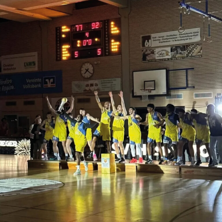 Ein Basketballteam jubelt freudig, trägt gelbe Trikots, umgeben von einer feierlichen Atmosphäre.